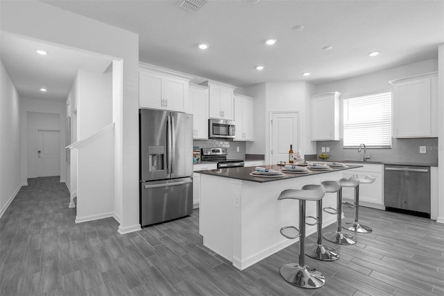 kitchen featuring appliances with stainless steel finishes, a kitchen bar, white cabinets, a center island, and wood finished floors