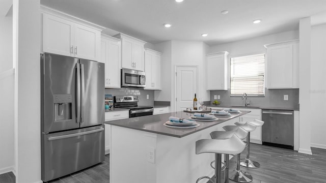 kitchen featuring appliances with stainless steel finishes, a sink, white cabinets, a breakfast bar, and recessed lighting