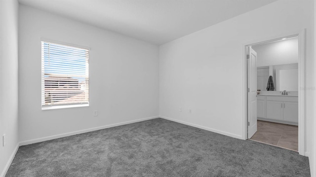 carpeted empty room featuring baseboards and a sink