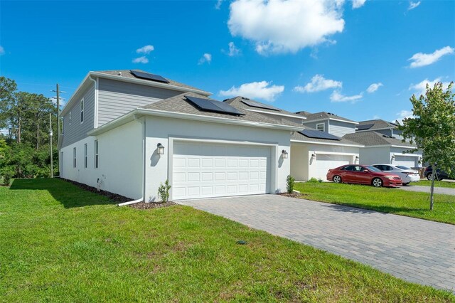 view of front facade with a garage, a front yard, decorative driveway, and solar panels