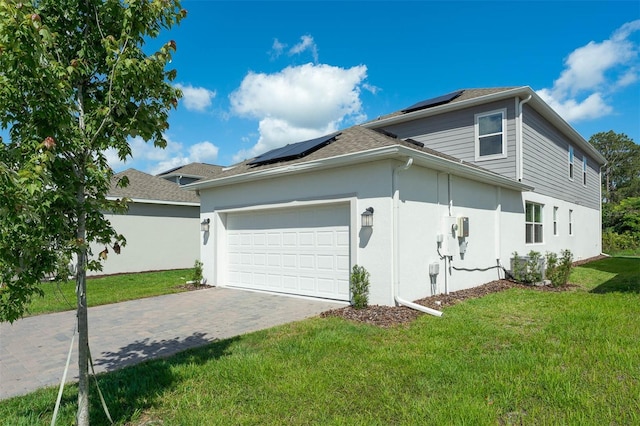 view of side of home with roof mounted solar panels, an attached garage, a lawn, driveway, and stucco siding