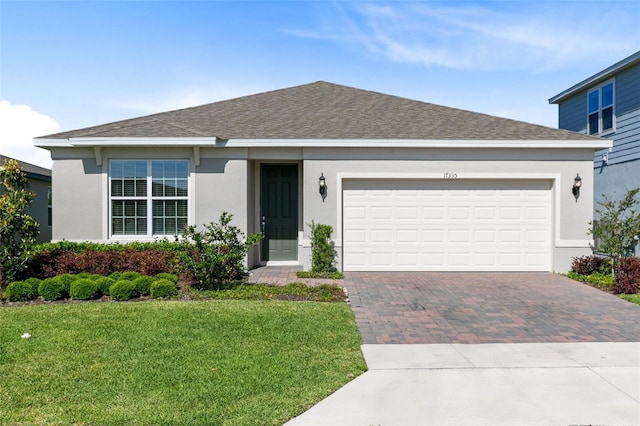 ranch-style house featuring decorative driveway, stucco siding, a front yard, a shingled roof, and an attached garage
