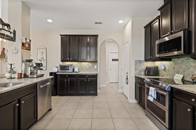 1501 Prairie Oaks Dr, Saint Cloud, FL 34771 - kitchen featuring stainless steel appliances, arched walkways, light stone countertops, light tile patterned floors, and decorative backsplash