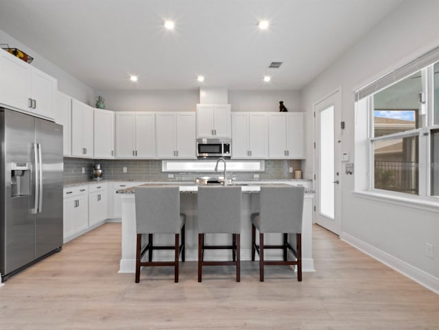 6875 Bridgman St, Orlando, FL 32827 - kitchen with stainless steel appliances, backsplash, a breakfast bar, a kitchen island with sink, and white cabinetry