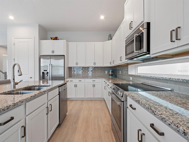6875 Bridgman St, Orlando, FL 32827 - kitchen featuring stainless steel appliances, a sink, light wood-type flooring, white cabinets, and tasteful backsplash