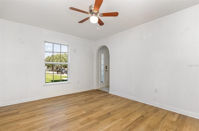 empty room featuring arched walkways, light wood-style floors, baseboards, and a ceiling fan