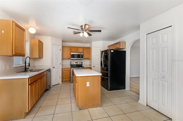 kitchen featuring appliances with stainless steel finishes, a sink, a ceiling fan, arched walkways, and a kitchen island