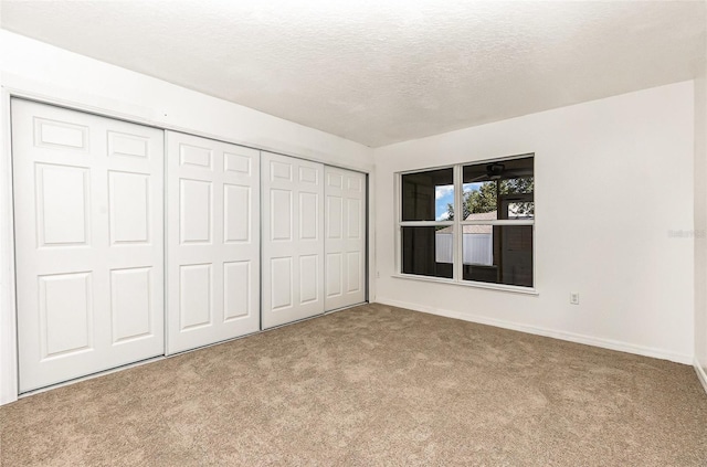 unfurnished bedroom with carpet, baseboards, a closet, and a textured ceiling
