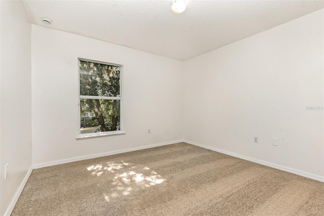 carpeted spare room featuring baseboards and a smoke detector