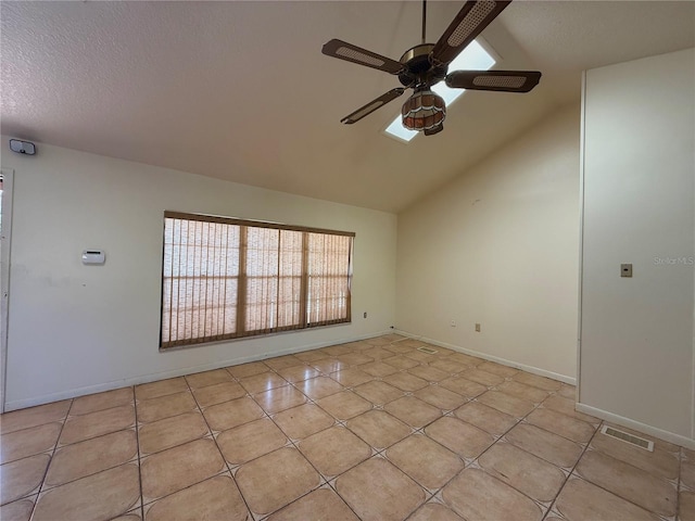 empty room with a ceiling fan, vaulted ceiling, light tile patterned floors, baseboards, and a textured ceiling