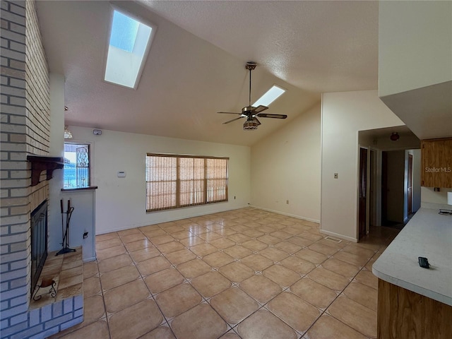 unfurnished living room featuring a skylight, lofted ceiling, ceiling fan, a fireplace, and light tile patterned flooring