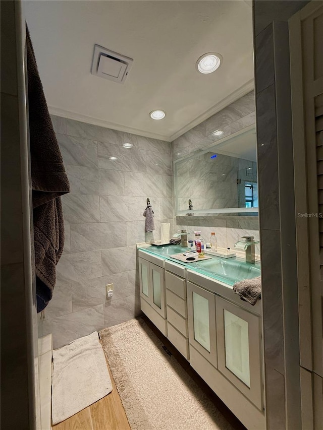 full bath with double vanity, tile walls, wood finished floors, crown molding, and recessed lighting