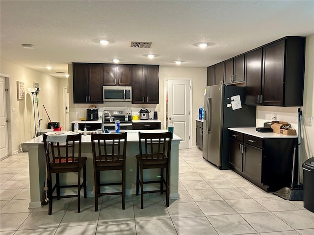 4427 Blackbird St, Kissimmee, FL 34746 - kitchen with appliances with stainless steel finishes, a kitchen breakfast bar, light tile patterned flooring, light countertops, and a textured ceiling