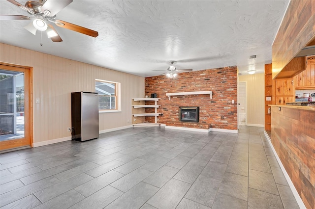 106 8th St, Lake Hamilton, FL 33851 - unfurnished living room with ceiling fan, wood walls, a brick fireplace, a textured ceiling, and baseboards