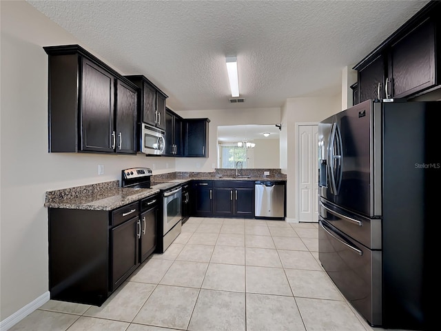 kitchen with appliances with stainless steel finishes, a sink, a textured ceiling, dark stone counters, and light tile patterned floors