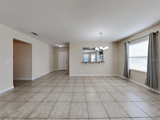 spare room with a chandelier, a textured ceiling, light tile patterned floors, and baseboards