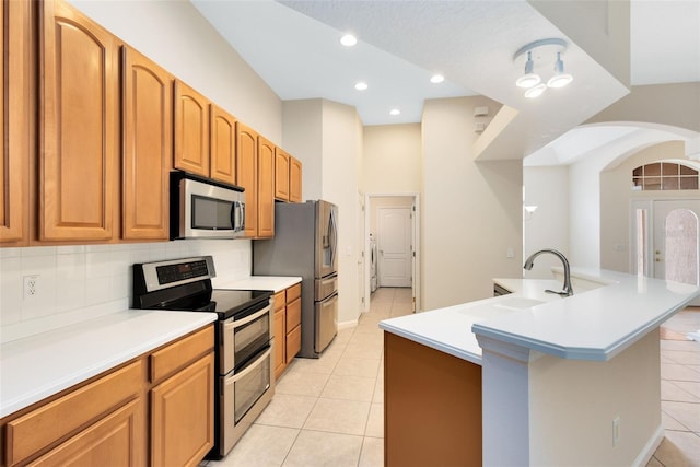 9330 Shadow Pinar Ct, Orlando, FL 32825 - kitchen featuring appliances with stainless steel finishes, a sink, light tile patterned floors, arched walkways, and a center island with sink