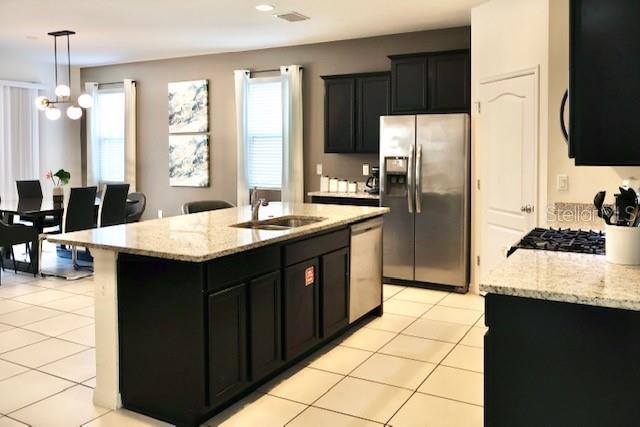 kitchen featuring appliances with stainless steel finishes, a sink, dark cabinetry, and light stone countertops