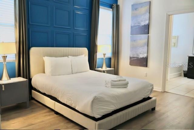 bedroom featuring light wood finished floors, baseboards, and ensuite bath
