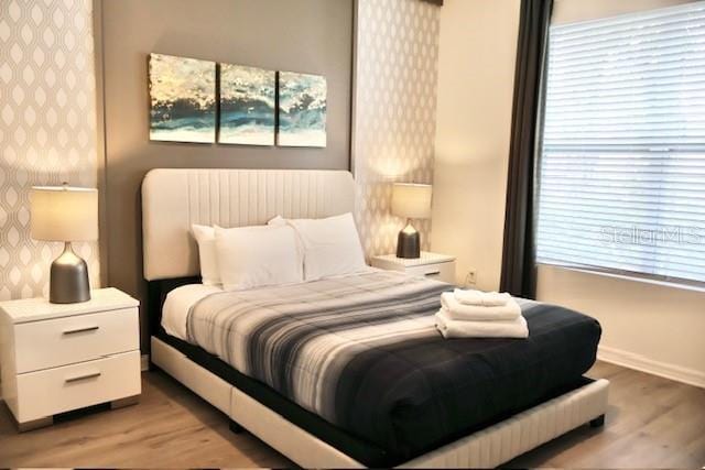 bedroom with wallpapered walls, light wood-style floors, baseboards, and multiple windows