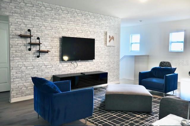 living room with wood finished floors, baseboards, and brick wall