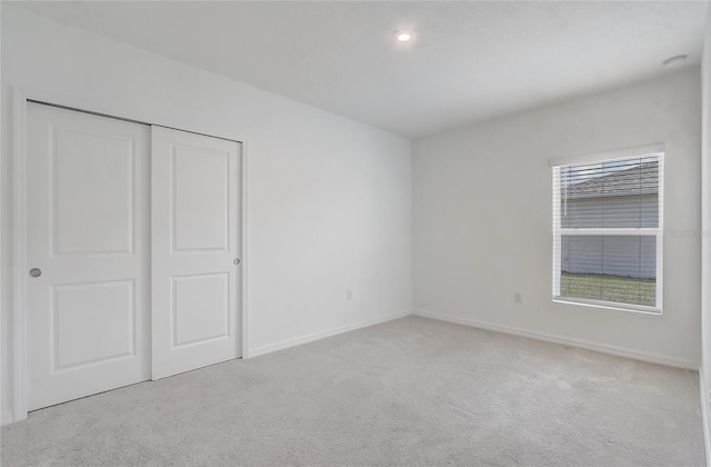 unfurnished bedroom with light colored carpet, baseboards, a closet, and recessed lighting