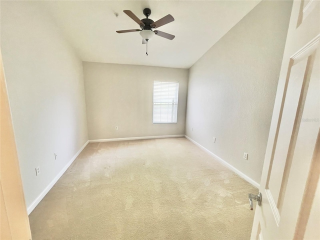spare room featuring a ceiling fan, light colored carpet, and baseboards