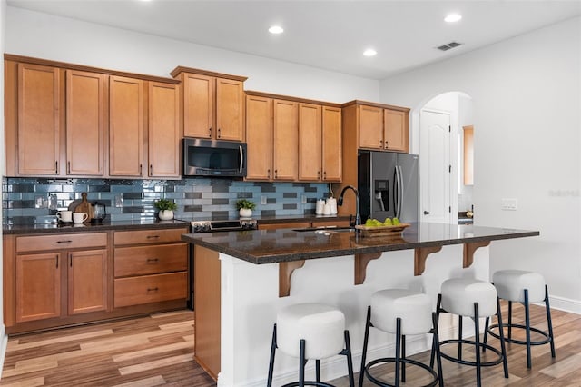 8692 Tavistock Lakes Blvd, Orlando, FL 32827 - kitchen featuring appliances with stainless steel finishes, brown cabinetry, arched walkways, tasteful backsplash, and recessed lighting