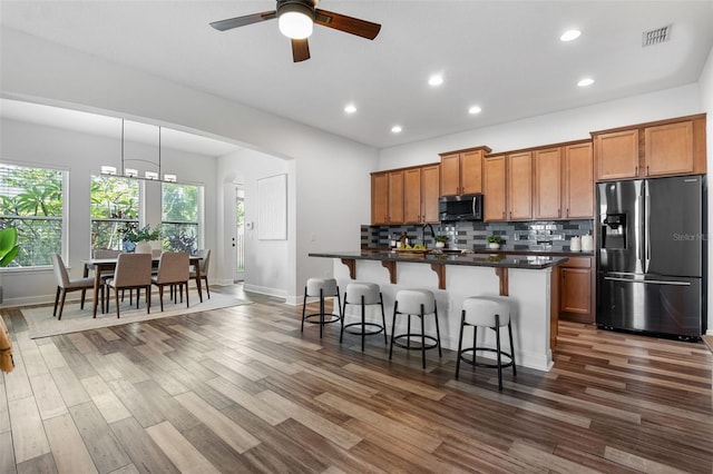 8692 Tavistock Lakes Blvd, Orlando, FL 32827 - kitchen featuring stainless steel appliances, brown cabinetry, a kitchen breakfast bar, dark countertops, and recessed lighting