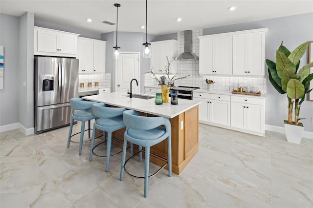 kitchen with stainless steel refrigerator with ice dispenser, wall chimney exhaust hood, a sink, baseboards, and decorative backsplash