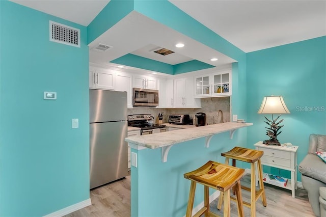 kitchen with appliances with stainless steel finishes, a breakfast bar area, light wood-style flooring, a peninsula, and recessed lighting