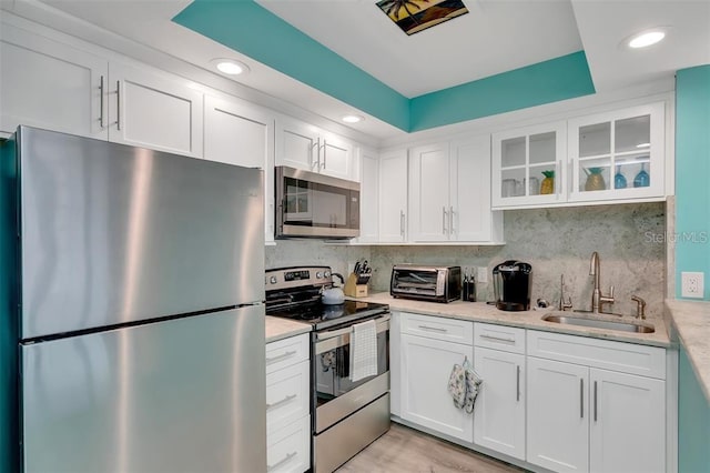 kitchen with appliances with stainless steel finishes, a sink, white cabinetry, light countertops, and decorative backsplash