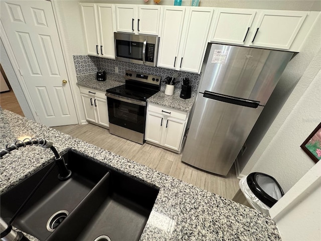 kitchen featuring stainless steel appliances, tasteful backsplash, a sink, light wood finished floors, and white cabinets
