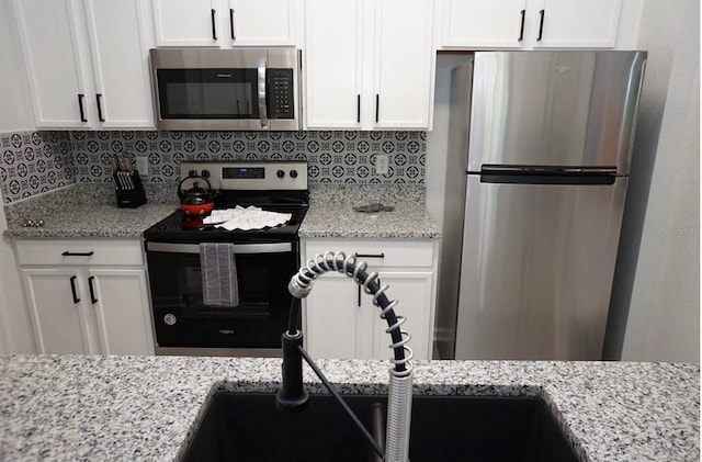 kitchen with appliances with stainless steel finishes, a sink, white cabinets, and decorative backsplash