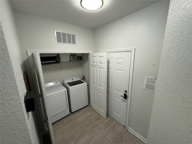 laundry room featuring independent washer and dryer, a textured wall, wood finished floors, and a textured ceiling