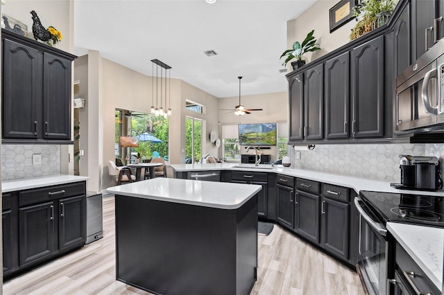 kitchen featuring stainless steel appliances, a sink, a peninsula, tasteful backsplash, and ceiling fan