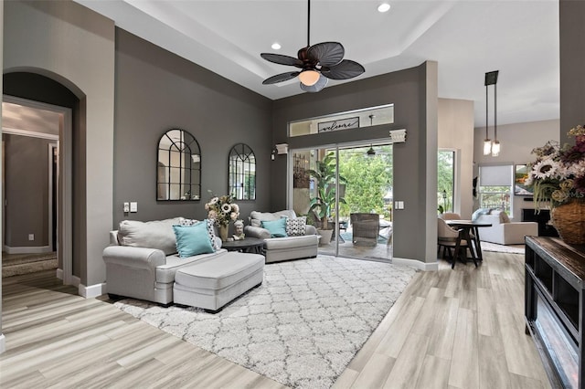 living room featuring wood finished floors, baseboards, a ceiling fan, a raised ceiling, and recessed lighting