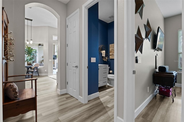 corridor featuring arched walkways, light wood-type flooring, and baseboards