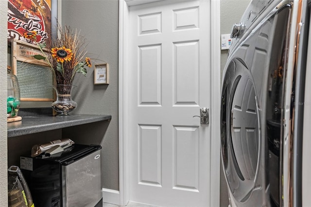 clothes washing area featuring a textured wall, washer / clothes dryer, and baseboards