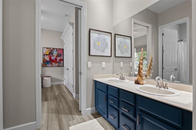 full bathroom with wood finished floors, double vanity, and baseboards