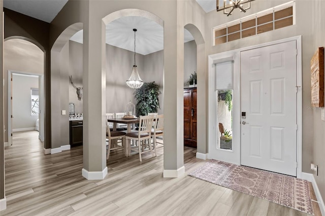 entryway featuring arched walkways, light wood-type flooring, a chandelier, and a towering ceiling