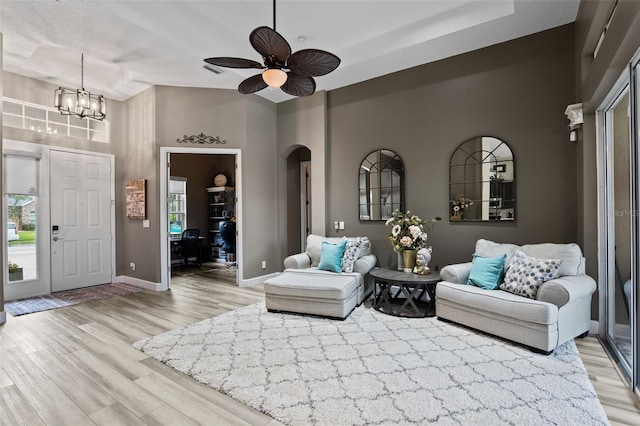 living area with arched walkways, light wood finished floors, baseboards, a high ceiling, and a chandelier