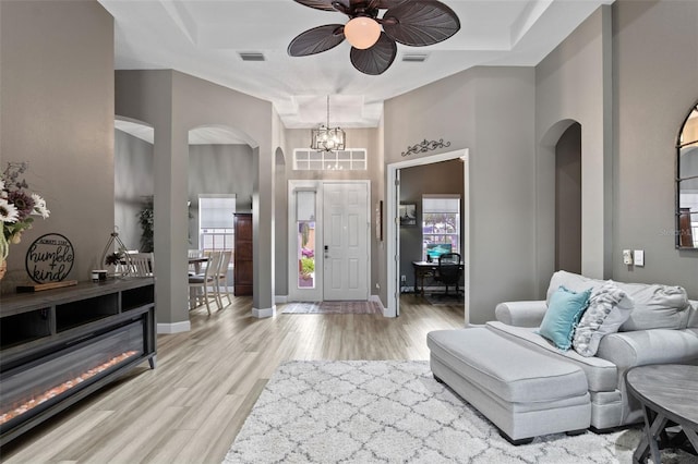 foyer with arched walkways, a ceiling fan, light wood-type flooring, baseboards, and a chandelier