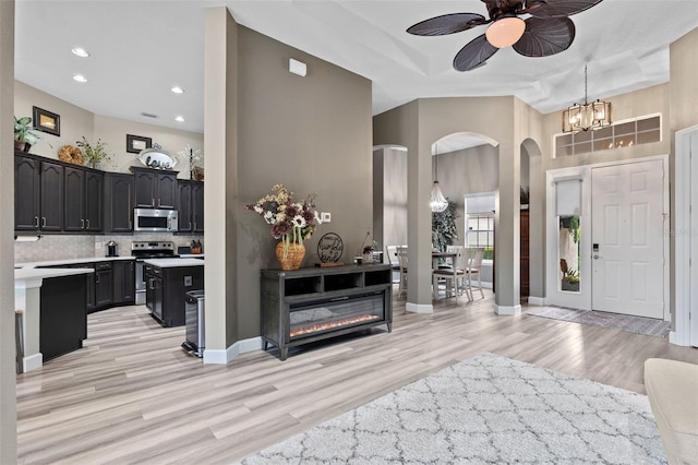 entrance foyer with ceiling fan, light wood-style floors, arched walkways, a chandelier, and a towering ceiling