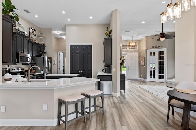 kitchen with appliances with stainless steel finishes, a chandelier, a sink, a peninsula, and light wood-style floors