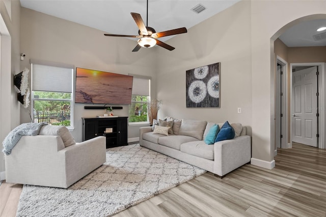 living room featuring arched walkways, a ceiling fan, light wood-type flooring, baseboards, and healthy amount of natural light