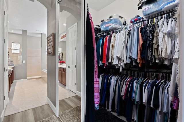 spacious closet with arched walkways and light wood-type flooring
