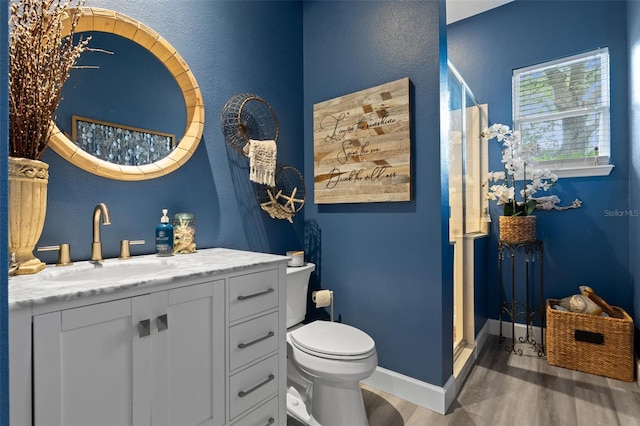 full bath featuring wood finished floors, a shower stall, vanity, toilet, and baseboards