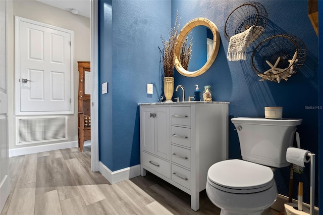 bathroom featuring toilet, wood finished floors, baseboards, vanity, and a textured wall
