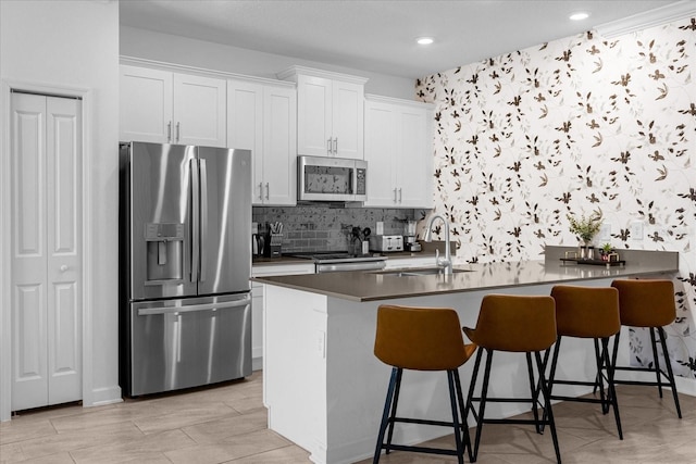 kitchen featuring stainless steel appliances, a sink, dark countertops, white cabinets, and a breakfast bar area